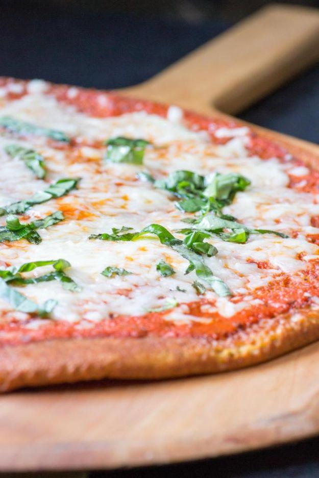 Thin and crispy quinoa crust pizza sliced on a board with melted cheese and a browned crisp golden edge