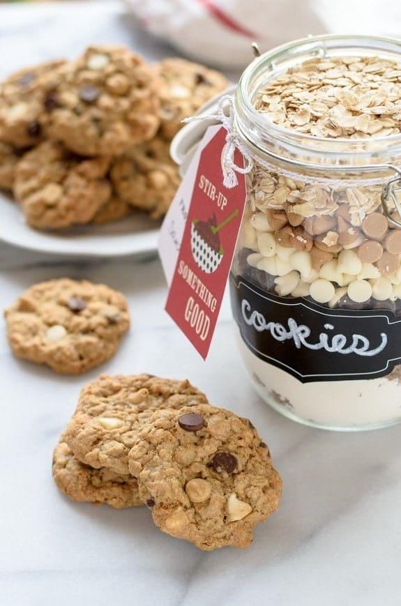 Glass jar layered with oats, chocolate and white chips beside baked cookies, labeled with a chalkboard cookies tag