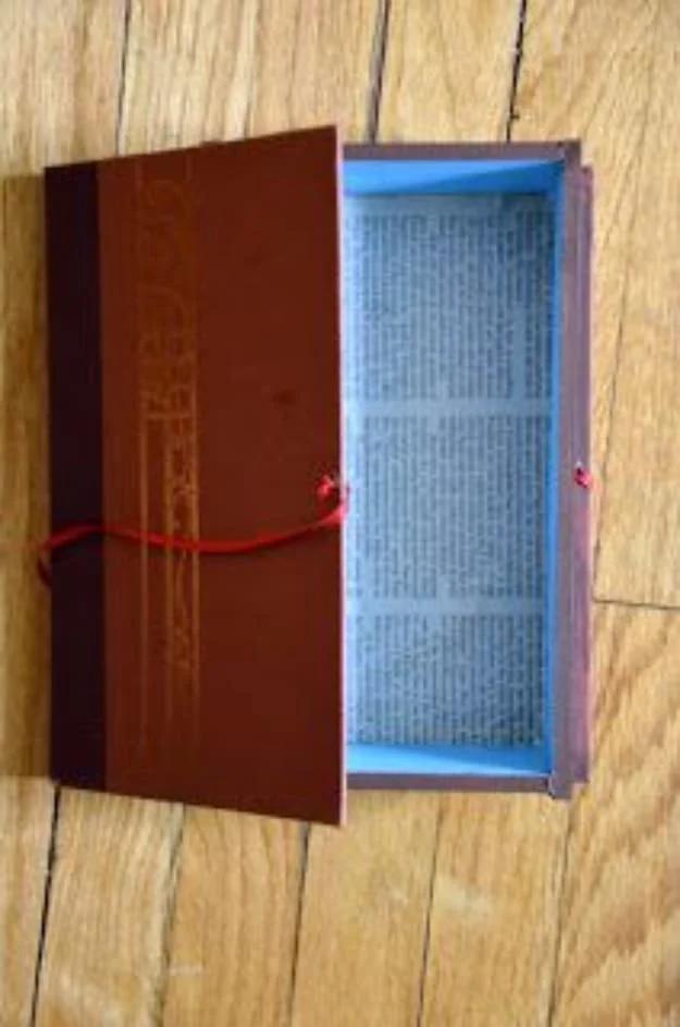Old book turned into a book box, opened flat on a wooden floor to show a blue painted wood lined compartment