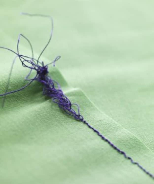 A tangled purple thread nest on the underside of green fabric, showing a sewing machine tension fault