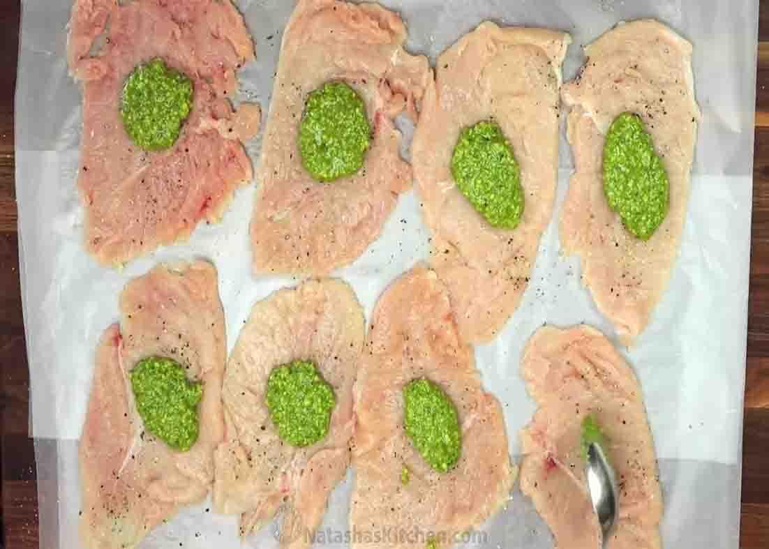 Spreading the pesto sauce over the chicken cutlets