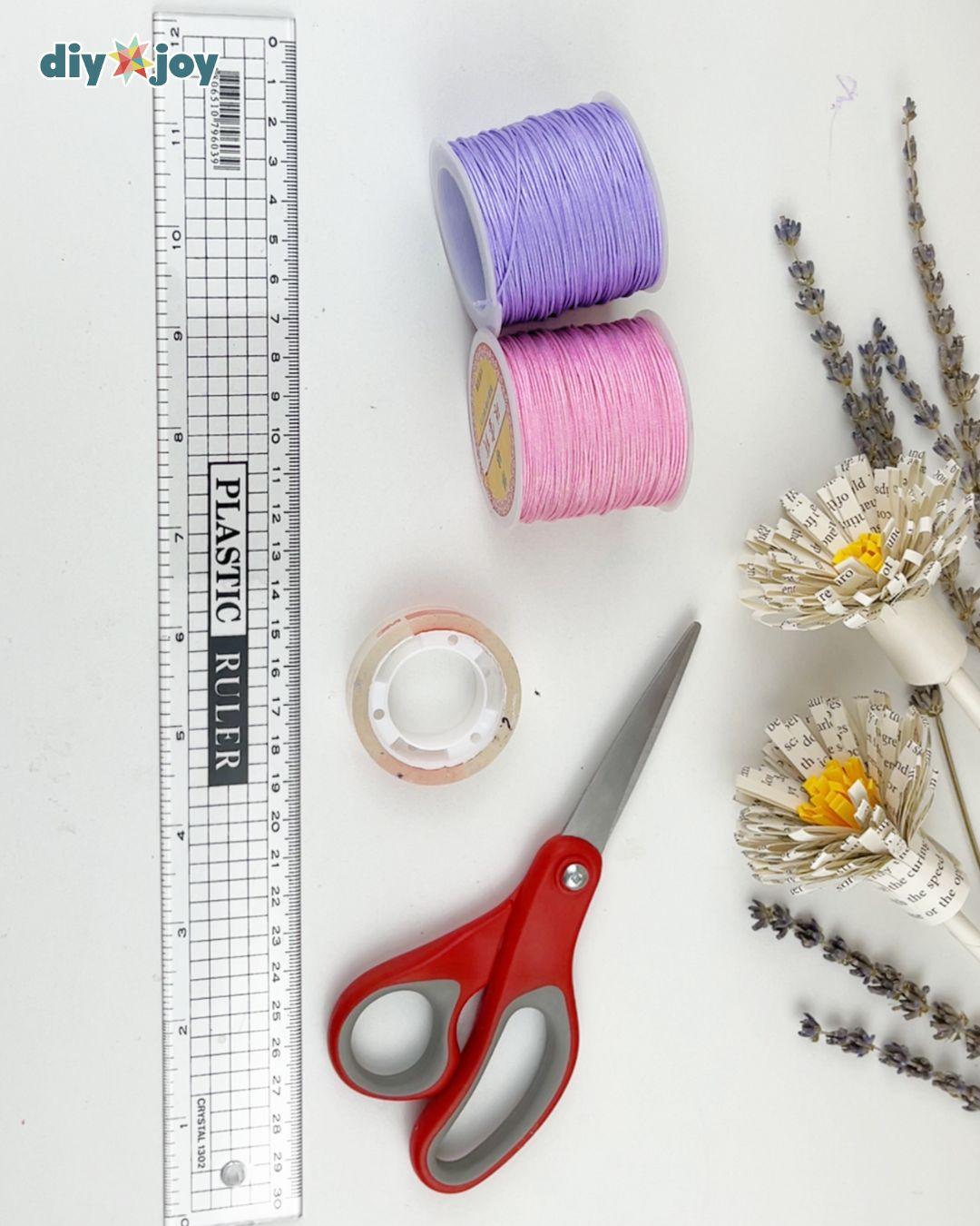 Macrame bracelet materials laid out, two colors of cord with scissors, measuring tape and tape to anchor the work
