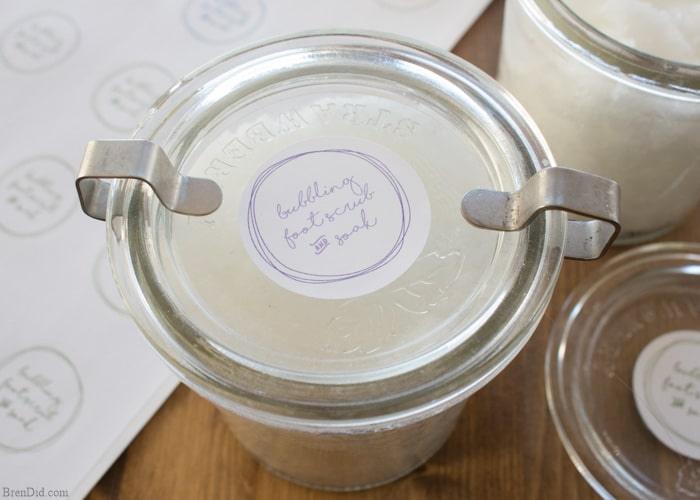 Bubbling foot scrub and soak, a glass clamp jar of pale salt scrub with a handwritten label beside matching jars