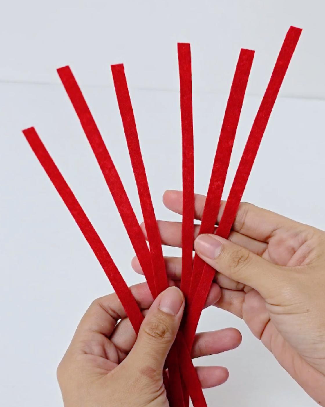 DIY Halloween Props - two hands holding a fan of red strips cut ready to wrap around the lollipop stick