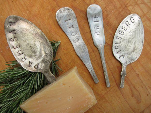 Four flattened silverware cheese markers stamped Parmesan, Goat, Brie and Jarlsberg on a wooden board