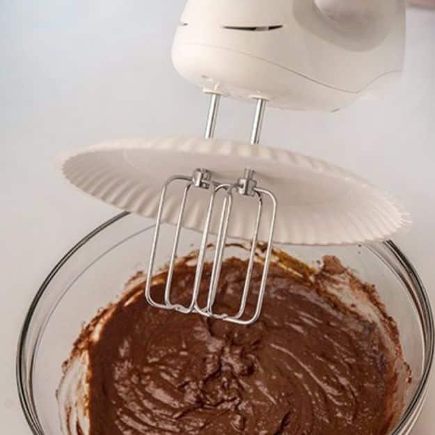 Hand mixer beaters pushed through a white paper plate and lowered into a glass bowl of chocolate cake batter
