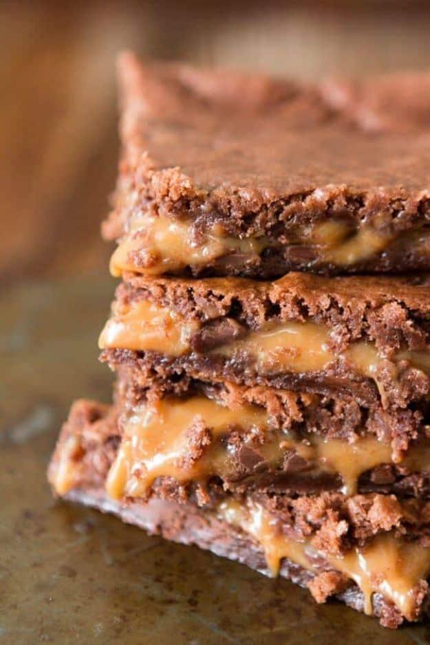 Caramel brownies stacked on a baking tray showing a thick molten caramel layer running through the middle