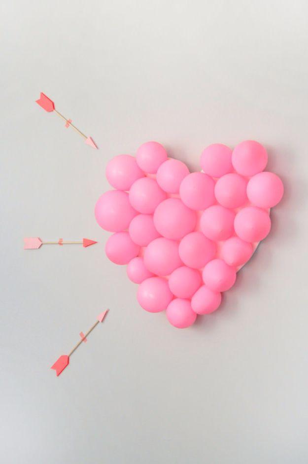 DIY balloon pop Valentine game with a foamcore heart covered in pink balloons and paper tipped dowel arrows