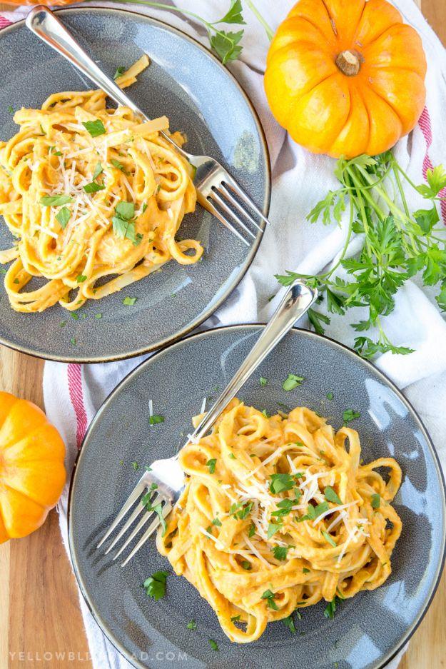 Two grey plates of fettuccine in creamy orange pumpkin alfredo sauce with forks and small orange pumpkins