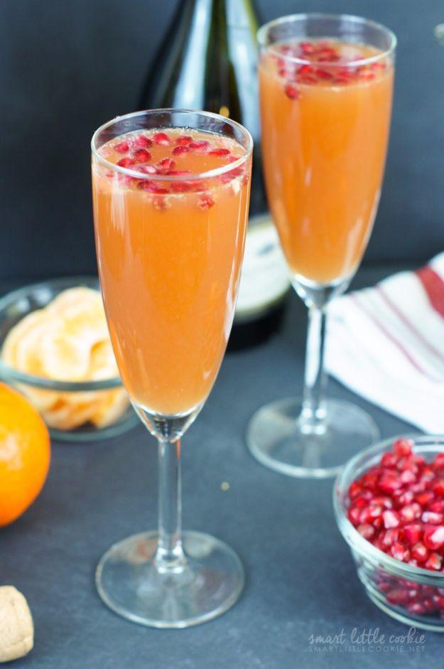 Two champagne flutes of tangerine pomegranate mimosa with pomegranate arils floating on top of the drink