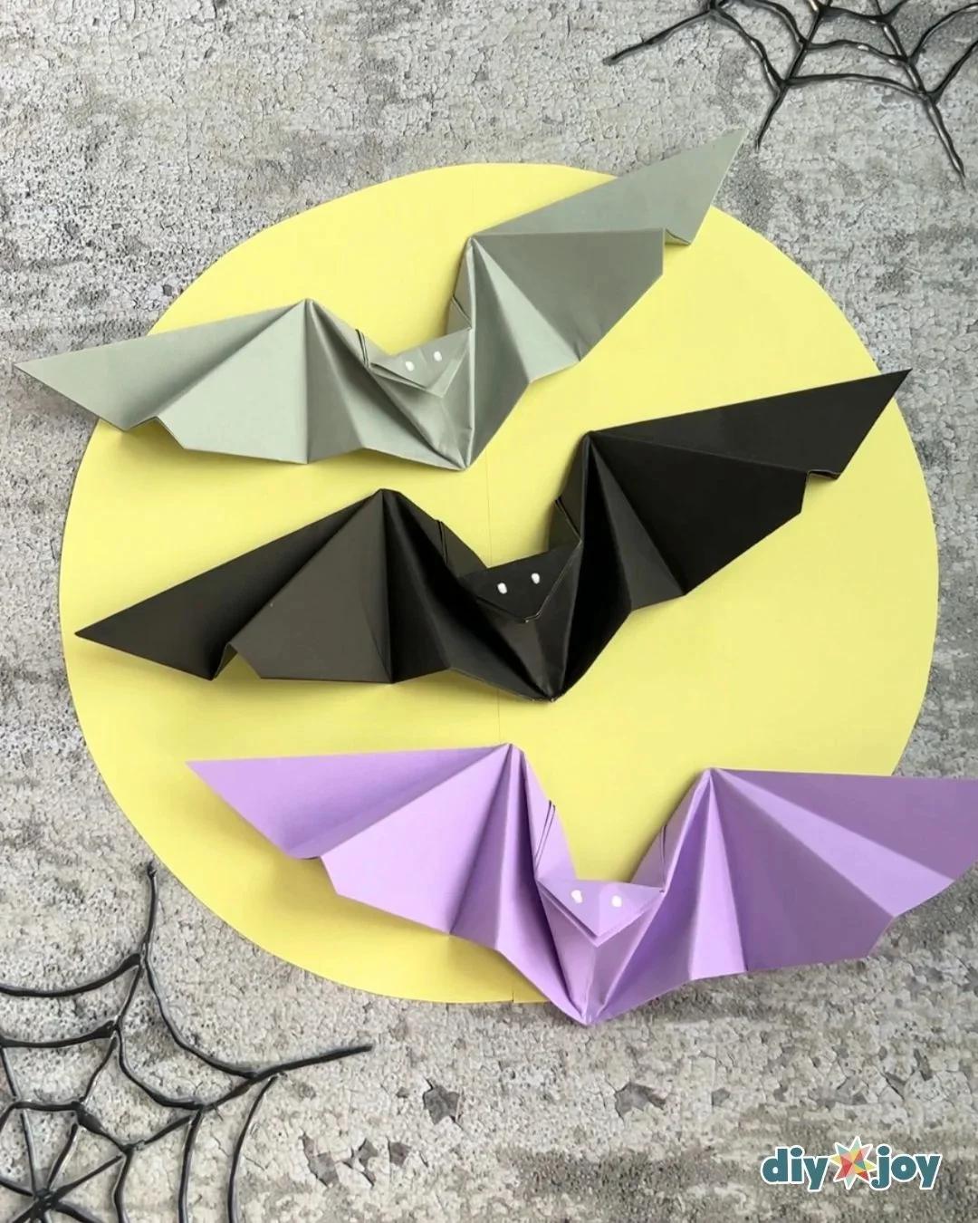 Paper bat with flapping wings held close up for Halloween, folded from a single square of origami paper.