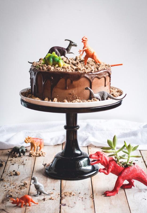 Chocolate dinosaur birthday cake topped with crushed cookie crumbs and small plastic toy dinosaurs on top