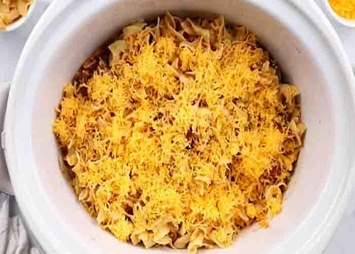 Adding the cheese to the slow cooker beef noodle casserole