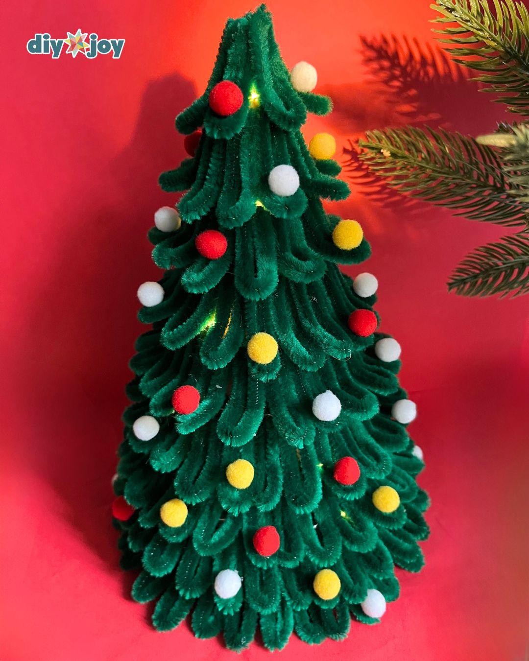 Christmas Tree Crafts - the tallest finished green pipe cleaner tree with pom poms and tiny warm fairy lights woven through the branches