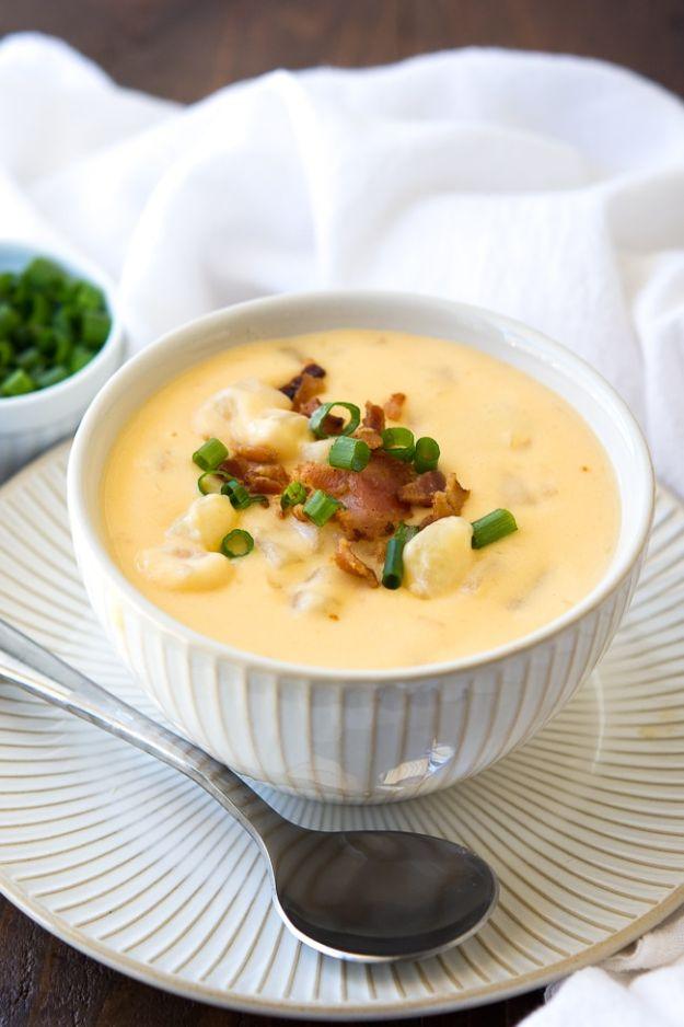 Crock pot cheesy potato soup in a white ribbed bowl and saucer, topped with bacon bits and green onions