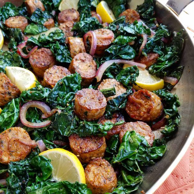 Lemon pepper chicken sausage and kale stir fry with browned sausage rounds, red onion and lemon wedges in a skillet