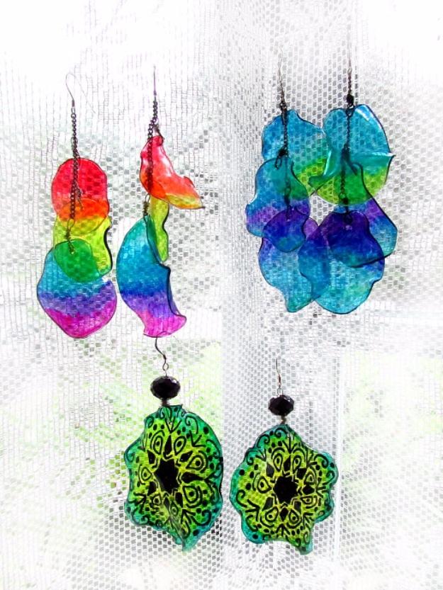 Three pairs of earrings made from shrunken plastic bottle pieces in rainbow and green tones, against white lace