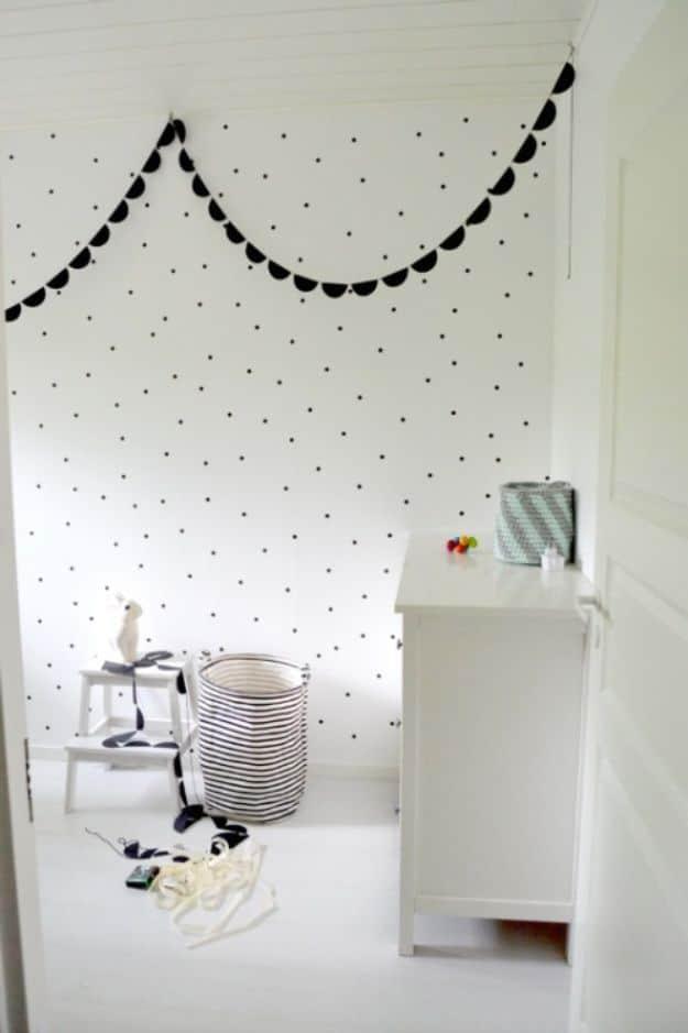 White nursery wall covered in small evenly spaced black polka dots, with a white dresser and a basket