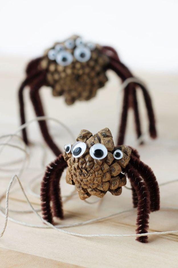 Two pine cone spiders with brown pipe cleaner legs and clusters of googly eyes, hanging on thread against a pale background