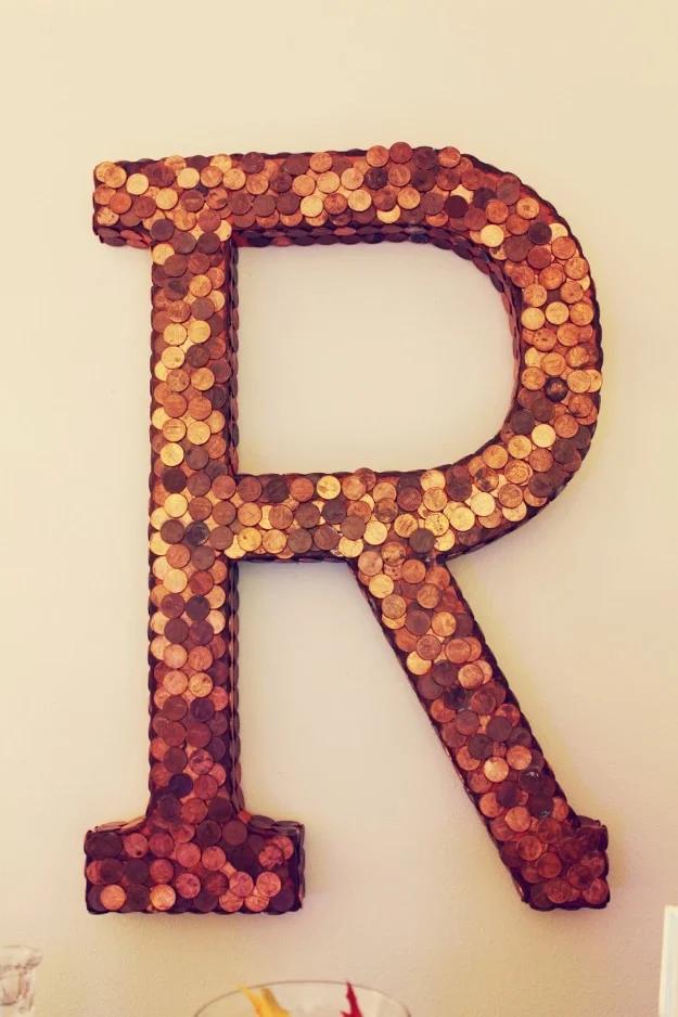 Penny craft monogram letter R covered in copper coins in varying shades, hung on a plain white bedroom wall
