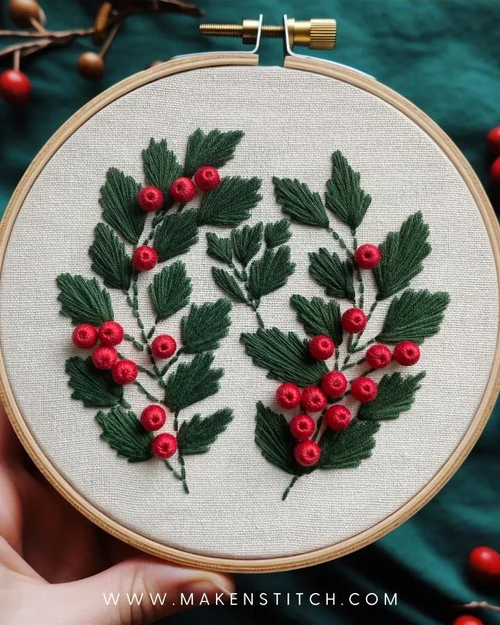 An embroidery hoop ornament of stitched mistletoe with green leaves and red bead berries on linen, held against green fabric