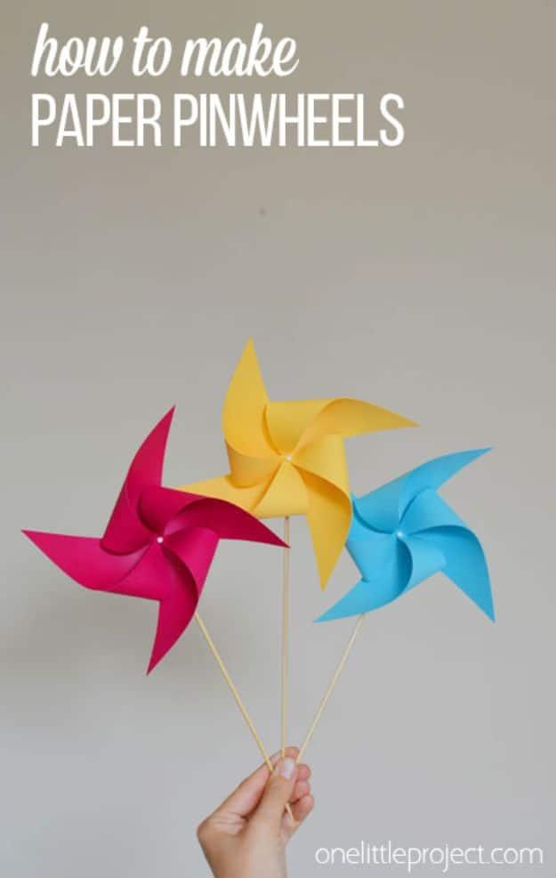 Hand holding three paper pinwheels in pink, yellow and blue on wooden skewers, under a typeset how to make title