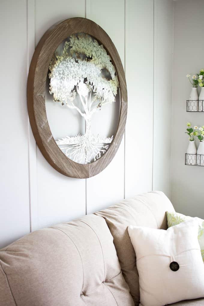 White board and batten accent wall with a large round wood framed mirror and white hydrangeas above a cream sofa