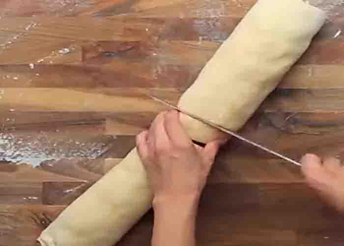 Slicing the dough roll to make the raspberry swirl buns