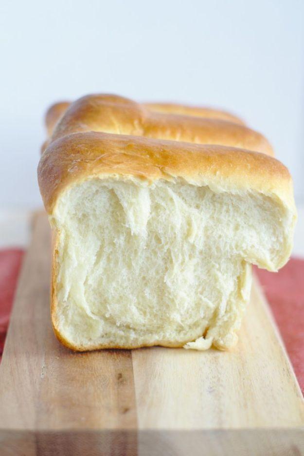 Tall white Hokkaido milk bread loaf with a rounded golden top sitting on a wooden board, one end pulled open