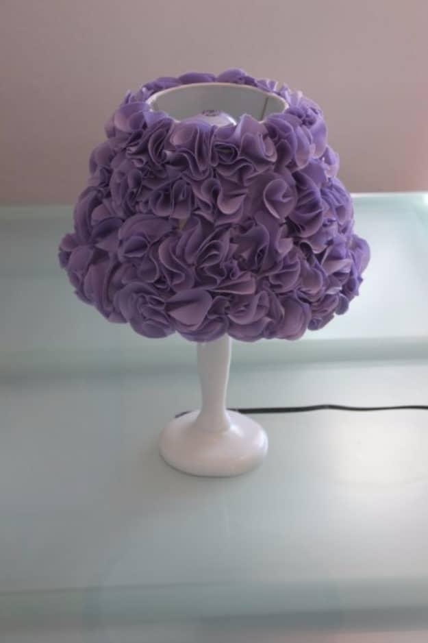 Table lamp with a shade completely covered in purple fabric pom poms on a white base, standing on a glass table