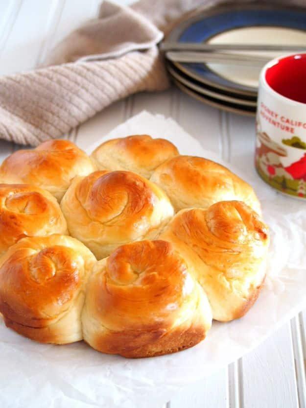 Soft milk bread rolls in a pan with a glossy egg washed top, pulled apart to show the fluffy soft layers