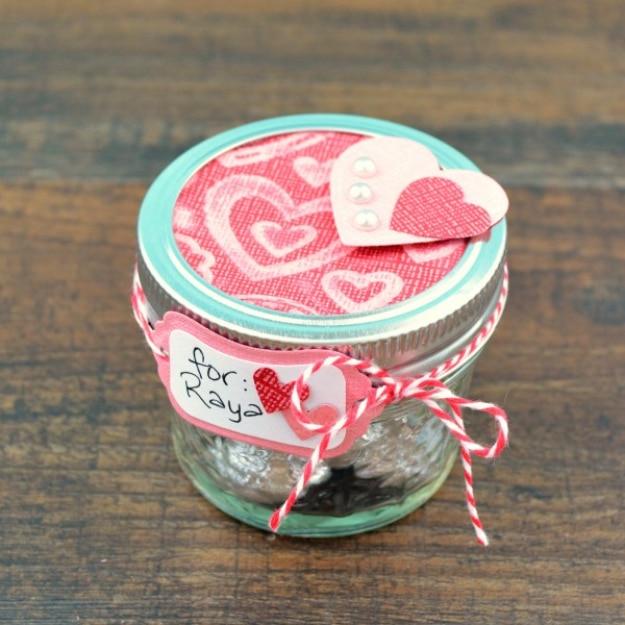 Hand decorated mini mason jar filled with small Valentine's Day candy treats and tied with ribbon for Valentine's Day