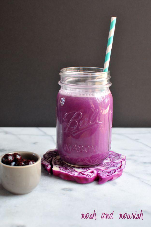 Super purple juice in a mason jar with a striped straw, a wedge of red cabbage and a bowl of blueberries