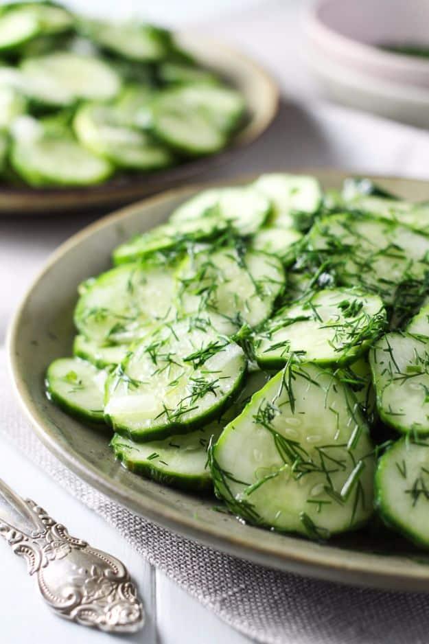 German cucumber salad, thin cucumber slices heavily flecked with fresh dill on a shallow green rimmed plate