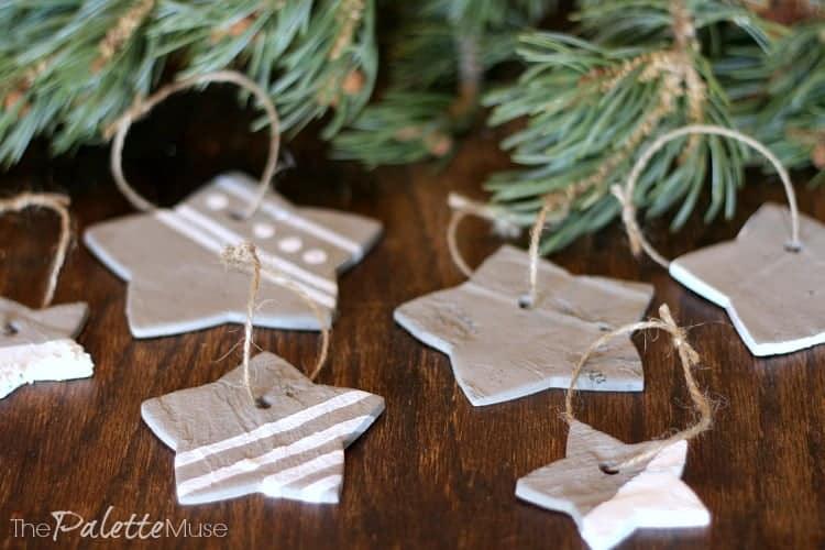 Five gray concrete star ornaments painted with thin white stripes and strung on twine beside pine branches