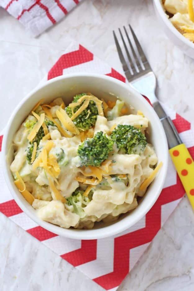 Broccoli mac and cheese in a small white bowl, florets stirred through creamy pasta and topped with shredded cheddar