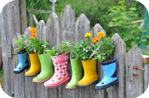 Rain boots gardening, seven small colorful wellington boots planted with marigolds hanging along a gray picket fence