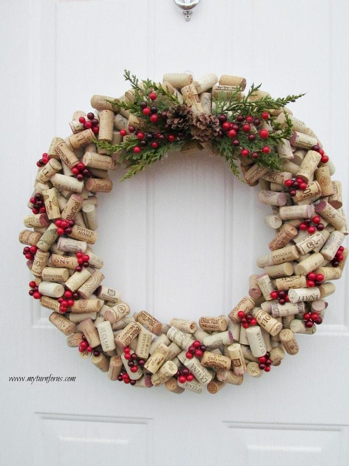 A wreath made entirely of wine corks glued in layers with cedar sprigs, two pinecones and red cranberry picks on a white door