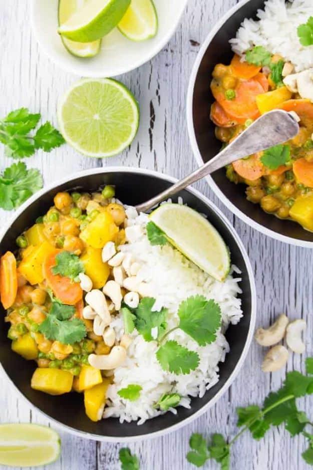 Two bowls of vegan chickpea curry with potatoes, carrots and peas served with white rice, lime and cashews