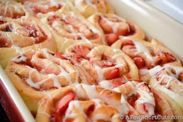 Pan of strawberry cinnamon rolls baked together and drizzled with white glaze, berries visible in the swirls