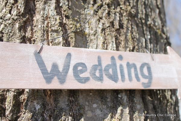 Weathered wooden arrow sign painted with the word Wedding in gray, nailed to the trunk of a large tree