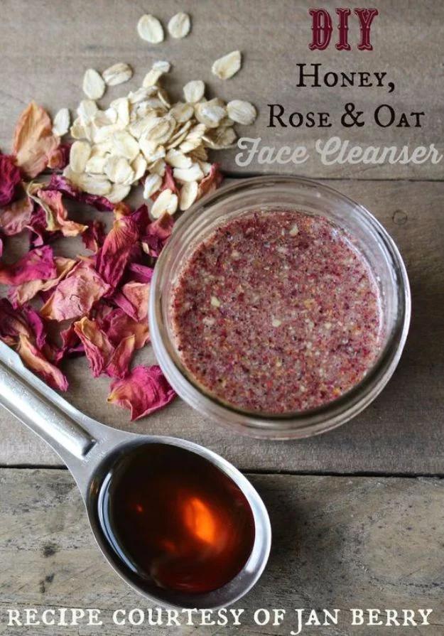 Honey rose petal oat face cleaner, a glass jar of reddish brown oat paste on wood beside a spoon of honey and dried petals