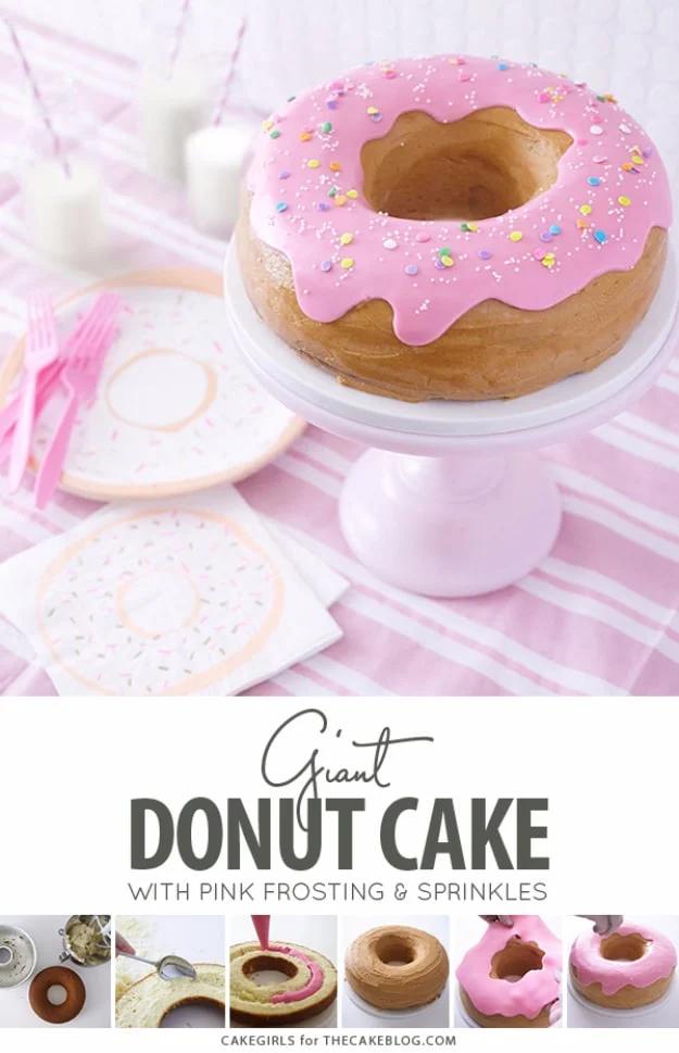 One giant donut shaped birthday cake with pink glaze and rainbow sprinkles on a pale pink cake stand