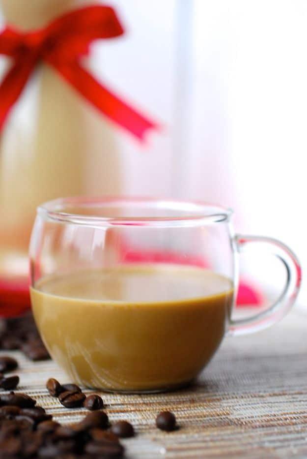 Coffee coquito poured into a clear glass mug, a ribboned bottle of the creamy drink and coffee beans behind