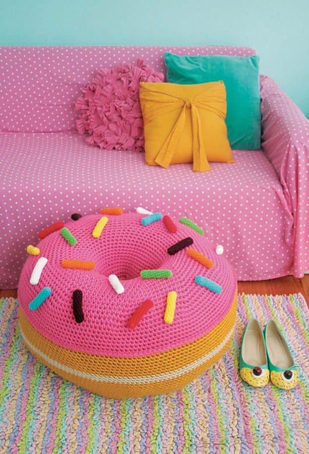 Giant crochet donut floor pouf with pink frosting, colorful sprinkles and a tan base sitting beside a pink daybed