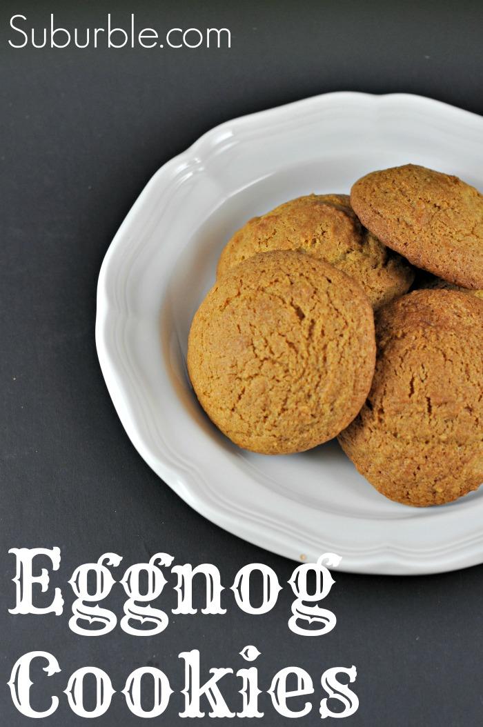 Golden brown puffy eggnog cookies piled on a white scalloped plate against a dark chalkboard background with the recipe title