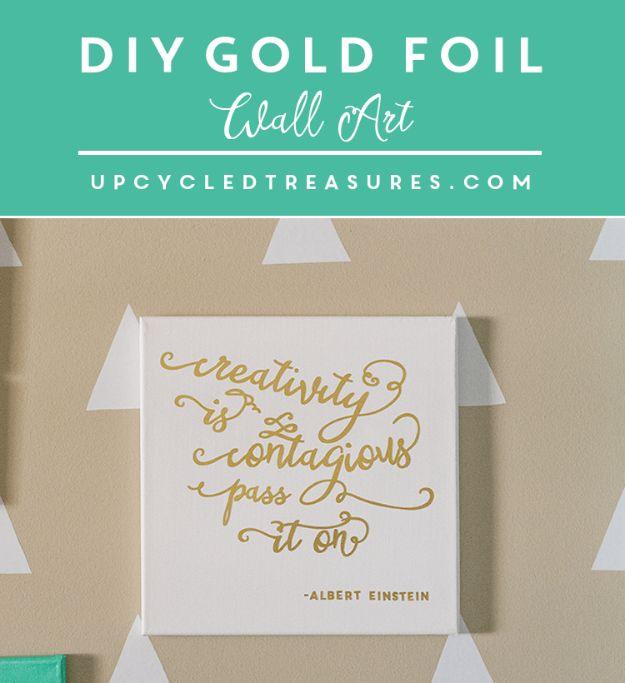 Gold foil hand lettered quote on a white square canvas hanging on a wall with pale gray geometric triangle paint