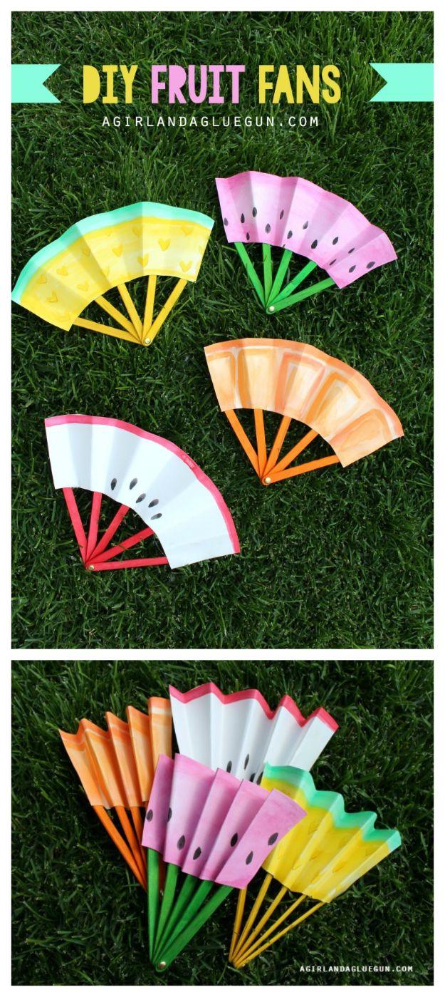 Paper fans painted as pineapple, watermelon and orange slices on colored popsicle sticks, laid on grass