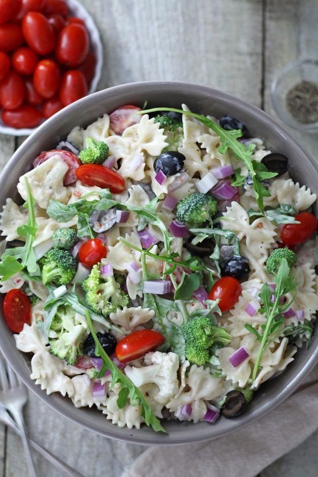 Creamy summer arugula pasta salad with bow ties, broccoli, cauliflower, olives and cherry tomatoes in a bowl