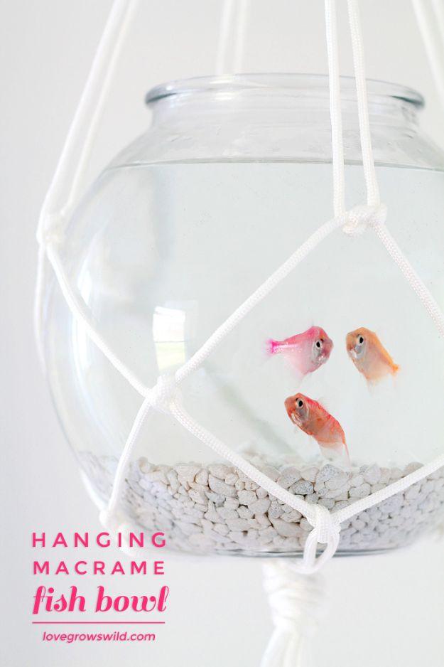 DIY aquarium bowl hanging in a knotted white macrame net, holding three orange fish above white gravel